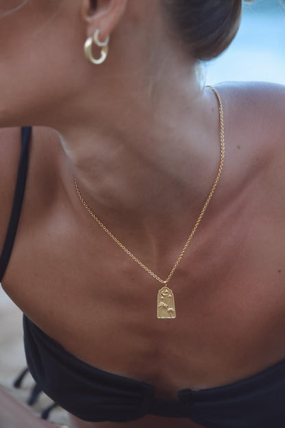 Model wearing Serene Scenes The Label 18K gold-filled Midnight Palm's Necklace. Gold chain with pendant featuring two palm trees under crescent moon and stars